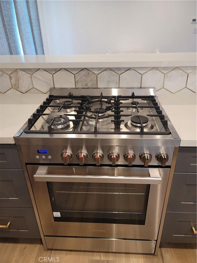 6091 Larchwood Dr, Huntington Beach, CA 92647 - detailed view of stainless steel stove, light countertops, decorative backsplash, and light wood finished floors