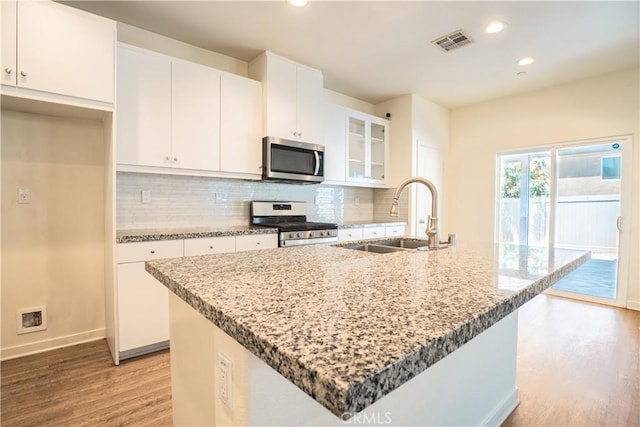 12893 Breccia Way, Moreno Valley, CA 92555 - kitchen with stainless steel appliances, light wood-style floors, white cabinets, an island with sink, and backsplash