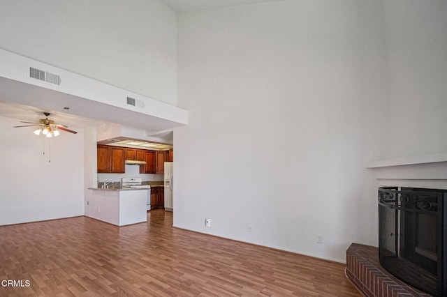 7211 Cozycroft Ave Unit 40, Winnetka, CA 91306 - unfurnished living room with a fireplace with raised hearth, wood finished floors, a ceiling fan, and a towering ceiling