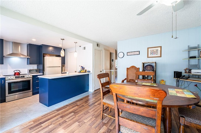 9739 Reseda Blvd Unit 36, Northridge, CA 91324 - kitchen with stainless steel range with electric stovetop, wall chimney exhaust hood, blue cabinets, white fridge, and a peninsula
