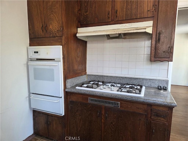 11505 Elmhurst Dr, Norwalk, CA 90650 - kitchen with white appliances, a warming drawer, under cabinet range hood, backsplash, and dark brown cabinetry