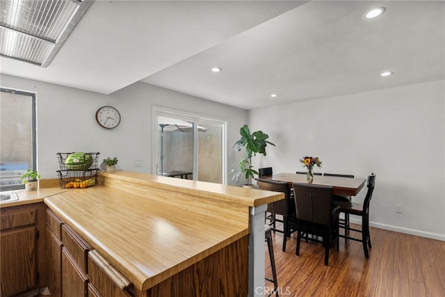 15230 Roxford St Unit 61, Sylmar, CA 91342 - kitchen featuring wood finished floors, recessed lighting, a peninsula, brown cabinets, and a kitchen breakfast bar