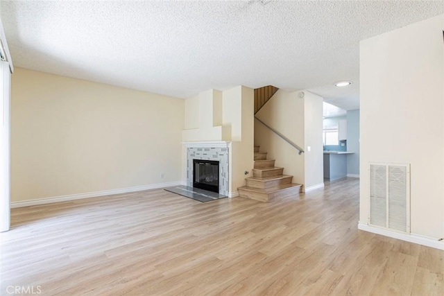 12411 Osborne St Unit 114, Pacoima, CA 91331 - unfurnished living room featuring light wood-style floors, a textured ceiling, a tile fireplace, and stairway