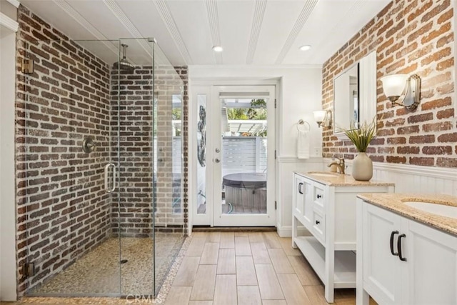 1780 Ocean Blvd, Pismo Beach, CA 93449 - bathroom featuring brick wall, two vanities, a shower stall, wainscoting, and wood finished floors