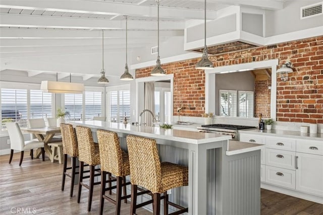 1780 Ocean Blvd, Pismo Beach, CA 93449 - kitchen featuring light countertops, brick wall, an island with sink, a breakfast bar, and dark wood finished floors