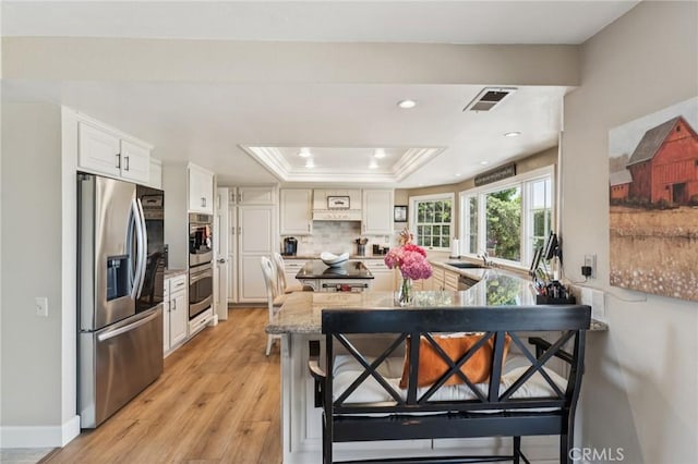 27201 Via Aurora, Mission Viejo, CA 92691 - kitchen featuring appliances with stainless steel finishes, a raised ceiling, light wood-style flooring, light stone countertops, and white cabinetry