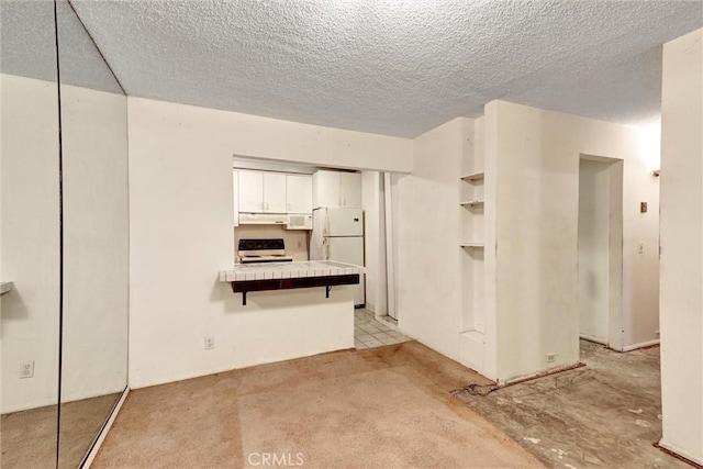 2600 Torrey Pines Rd Unit A13, La Jolla, CA 92037 - kitchen with freestanding refrigerator, stove, under cabinet range hood, white cabinetry, and a peninsula