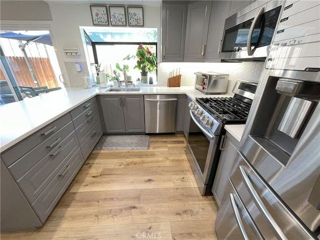 9749 Reseda Blvd Unit 13, Northridge, CA 91324 - kitchen with gray cabinetry, stainless steel appliances, light wood-type flooring, decorative backsplash, and light countertops