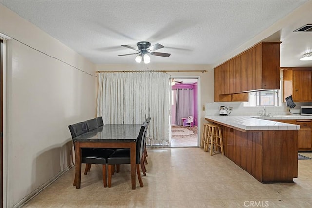 260 E Whittier Ave, Hemet, CA 92543 - kitchen featuring tile counters, brown cabinets, stainless steel microwave, ceiling fan, and a peninsula