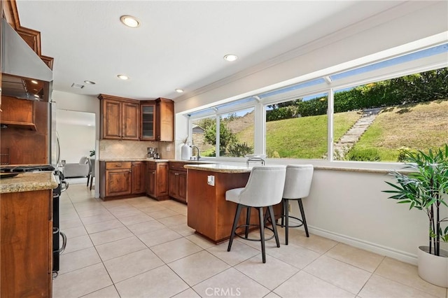 20681 Via Amarilla, Yorba Linda, CA 92886 - kitchen featuring under cabinet range hood, stove, brown cabinetry, a breakfast bar, and light tile patterned floors