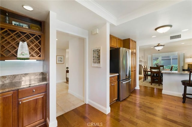 5185 Duenas, Laguna Woods, CA 92637 - kitchen featuring freestanding refrigerator, brown cabinets, dark wood-type flooring, crown molding, and light stone countertops