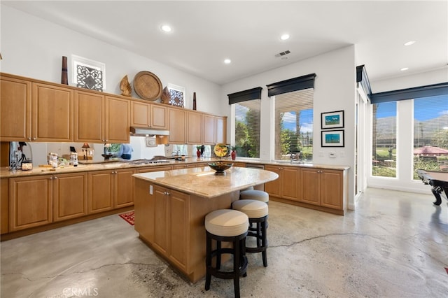 56102 Baltusrol Ln, Quinta, CA 92253 - kitchen with finished concrete flooring, under cabinet range hood, a kitchen island, stainless steel gas cooktop, and a breakfast bar