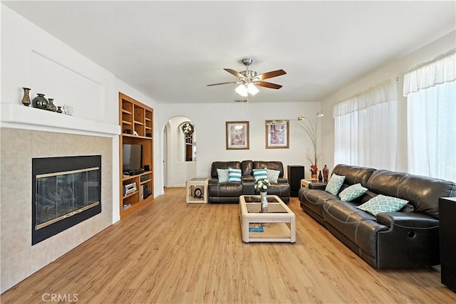 9790 Heatherhearst Dr, Chowchilla, CA 93610 - living room featuring wood finished floors, a ceiling fan, built in features, arched walkways, and a tiled fireplace