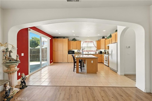 9790 Heatherhearst Dr, Chowchilla, CA 93610 - kitchen featuring white refrigerator with ice dispenser, arched walkways, gas range oven, a breakfast bar area, and plenty of natural light