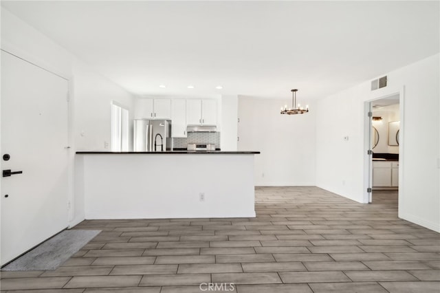 2827 S Fairview St Unit O, Santa Ana, CA 92704 - kitchen featuring freestanding refrigerator, a chandelier, under cabinet range hood, dark countertops, and white cabinetry