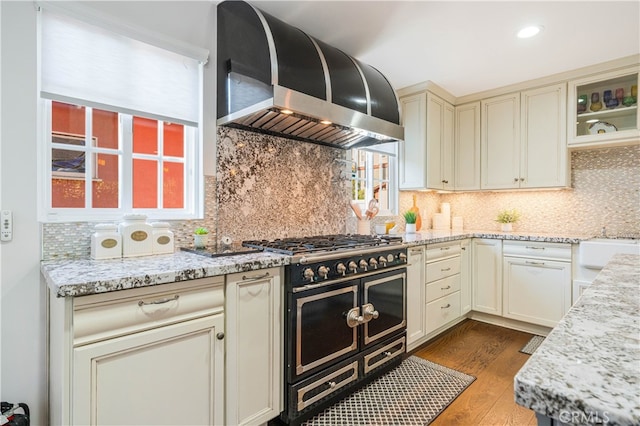 4022 Willowcrest Ave, Studio City, CA 91604 - kitchen featuring wall chimney exhaust hood, range with two ovens, cream cabinetry, wood finished floors, and decorative backsplash