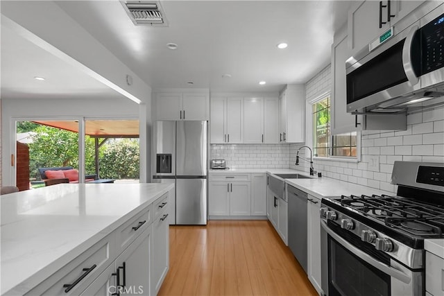 17172 Lahey St, Granada Hills, CA 91344 - kitchen with stainless steel appliances, backsplash, light wood-style flooring, white cabinets, and recessed lighting