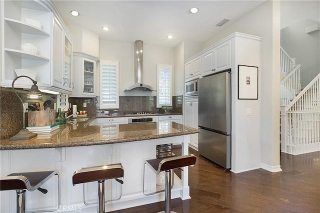 6 Via Amanti, Newport Coast, CA 92657 - kitchen with appliances with stainless steel finishes, wall chimney exhaust hood, a peninsula, dark wood finished floors, and dark stone countertops