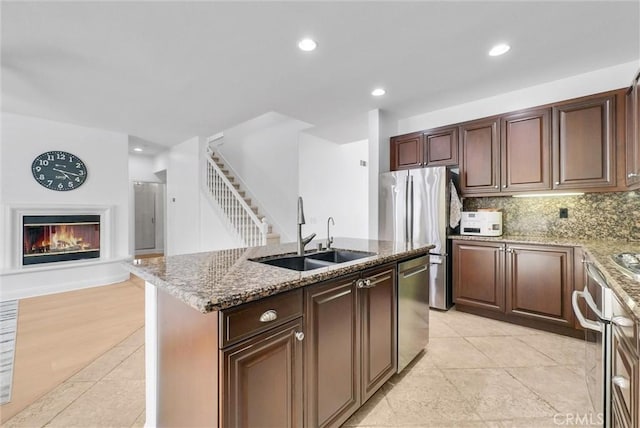 7059 E Monaco, Orange, CA 92867 - kitchen with appliances with stainless steel finishes, a glass covered fireplace, light stone counters, backsplash, and an island with sink