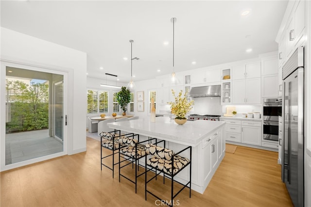 56 Cartwheel, Irvine, CA 92618 - kitchen with stainless steel appliances, ventilation hood, white cabinetry, light wood finished floors, and a kitchen breakfast bar