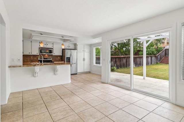 10559 Lansford Ln, San Diego, CA 92126 - kitchen with appliances with stainless steel finishes, a peninsula, tasteful backsplash, light tile patterned flooring, and dark stone counters