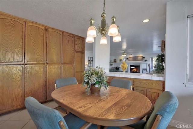18032 Ohna Rd, Apple Valley, CA 92307 - dining area featuring a chandelier, light tile patterned floors, a lit fireplace, and ceiling fan