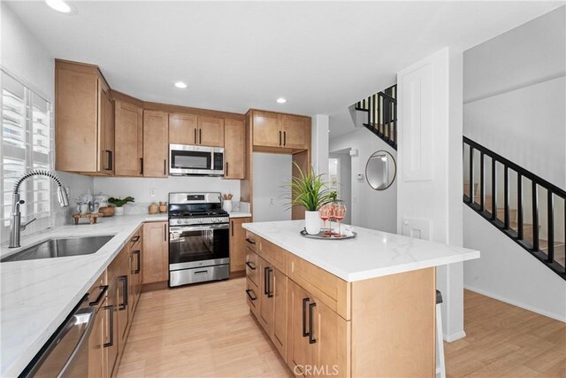 2 Chestnut Dr, Aliso Viejo, CA 92656 - kitchen featuring stainless steel appliances, light wood-style flooring, light stone counters, brown cabinetry, and a center island