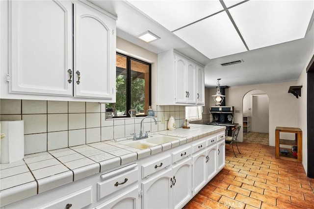 31039 Hasley Canyon Rd, Castaic, CA 91384 - kitchen featuring arched walkways, tile counters, white cabinets, and backsplash