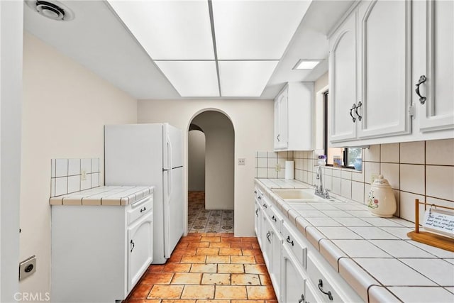 31039 Hasley Canyon Rd, Castaic, CA 91384 - kitchen featuring tile counters, arched walkways, freestanding refrigerator, tasteful backsplash, and white cabinetry
