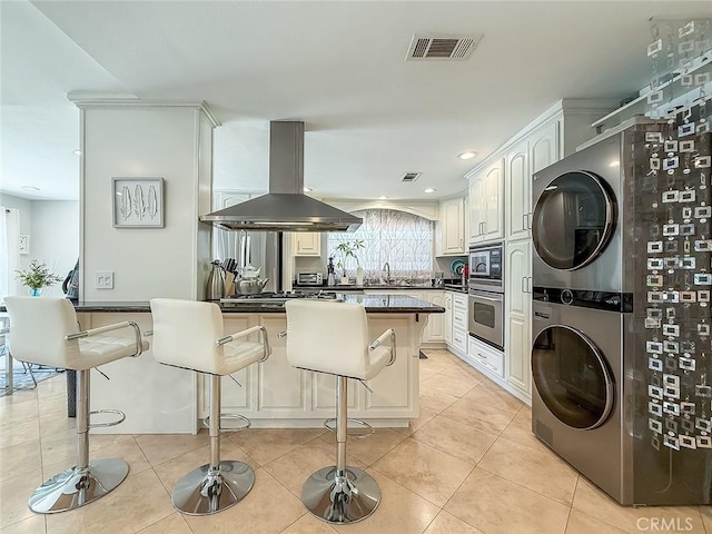 24017 Sylvan St, Woodland Hills, CA 91367 - kitchen featuring island range hood, stacked washing machine and dryer, stainless steel appliances, a kitchen bar, and dark countertops