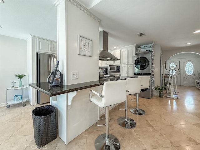24017 Sylvan St, Woodland Hills, CA 91367 - kitchen featuring appliances with stainless steel finishes, wall chimney range hood, stacked washer and clothes dryer, arched walkways, and a breakfast bar area