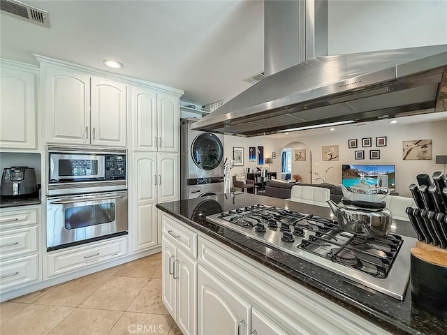 24017 Sylvan St, Woodland Hills, CA 91367 - kitchen featuring stainless steel appliances, stacked washer / drying machine, wall chimney exhaust hood, light tile patterned floors, and open floor plan