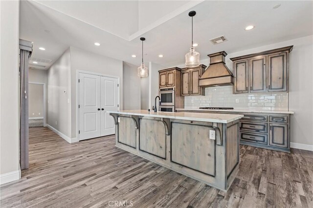 21813 Valley Vista Dr, Tehachapi, CA 93561 - kitchen with custom range hood, gas stovetop, wood finished floors, an island with sink, and recessed lighting