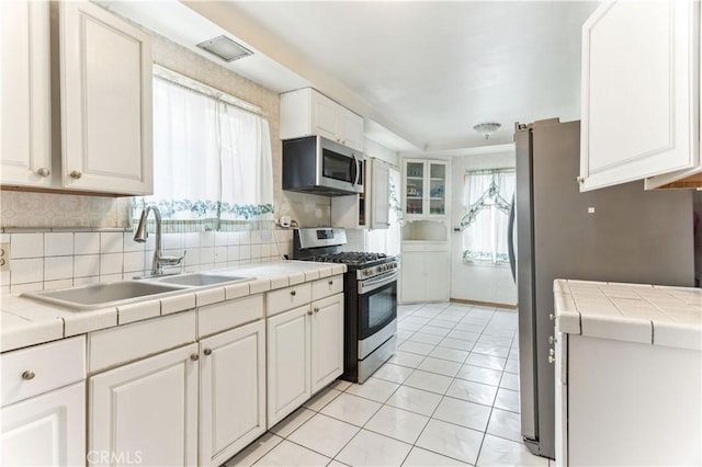 4519 9th Ave, Los Angeles, CA 90043 - kitchen with appliances with stainless steel finishes, tile counters, white cabinetry, tasteful backsplash, and light tile patterned flooring