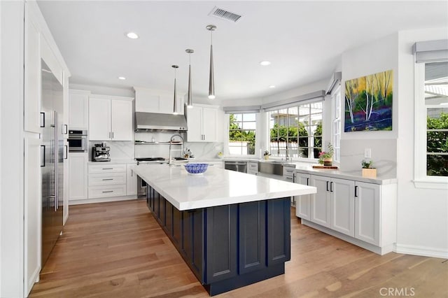 29614 Ridgeway Dr, Agoura Hills, CA 91301 - kitchen with light countertops, white cabinets, a kitchen island with sink, light wood-type flooring, and pendant lighting