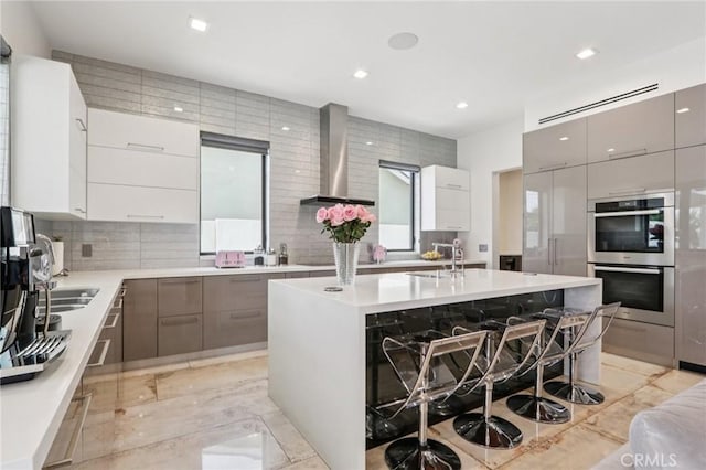 10418 Rubio Ave, Granada Hills, CA 91344 - kitchen with wall chimney exhaust hood, modern cabinets, double oven, decorative backsplash, and a kitchen breakfast bar