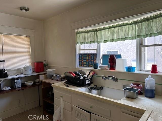1045 Gladys Ave, Long Beach, CA 90804 - kitchen with tile countertops, white cabinetry, and healthy amount of natural light