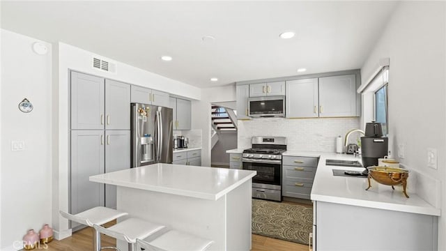 23208 Cuervo Dr, Valencia, CA 91354 - kitchen featuring appliances with stainless steel finishes, gray cabinets, light wood finished floors, decorative backsplash, and a kitchen island
