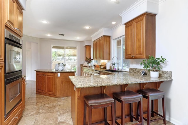 13748 Torrey Glenn Rd, San Diego, CA 92129 - kitchen featuring double oven, brown cabinetry, light stone countertops, a center island, and crown molding