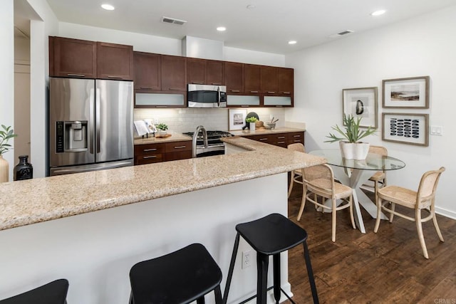 10667 Golden Willow Unit 152, San Diego, CA 92130 - kitchen featuring stainless steel appliances, a kitchen breakfast bar, decorative backsplash, dark wood-style flooring, and light stone counters