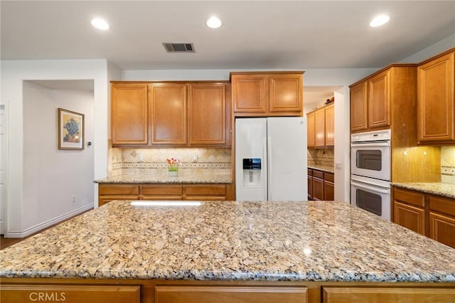 6411 Puma Pl, Rancho Cucamonga, CA 91737 - kitchen with white appliances, a center island, light stone counters, brown cabinets, and recessed lighting