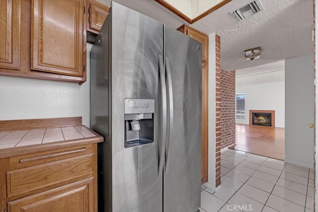 20155 Keswick St Unit 211, Winnetka, CA 91306 - kitchen with stainless steel fridge with ice dispenser, tile countertops, light tile patterned floors, a textured ceiling, and a glass covered fireplace