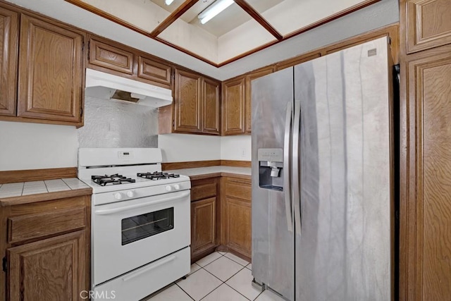 20155 Keswick St Unit 211, Winnetka, CA 91306 - kitchen with stainless steel fridge, white range with gas cooktop, range hood, tile counters, and brown cabinetry