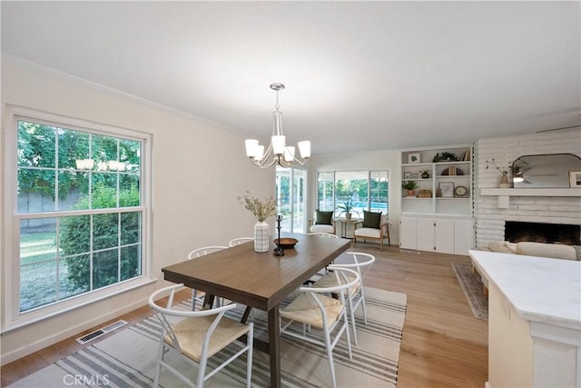 6330 N Wilson Ave, Fresno, CA 93704 - dining space featuring a chandelier, plenty of natural light, light wood-type flooring, a brick fireplace, and ornamental molding