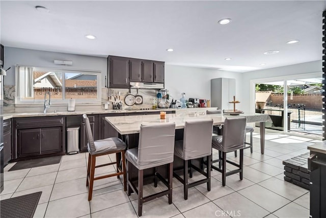 43657 21st St W, Lancaster, CA 93536 - kitchen featuring a kitchen breakfast bar, tasteful backsplash, under cabinet range hood, light stone countertops, and dark brown cabinets