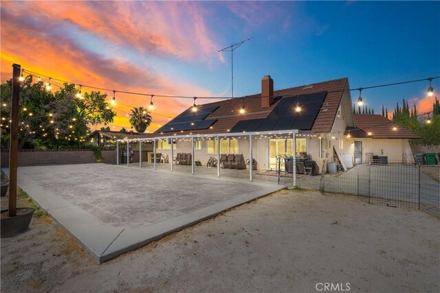 43657 21st St W, Lancaster, CA 93536 - back of property at dusk featuring a patio, solar panels, a chimney, a fenced backyard, and stucco siding