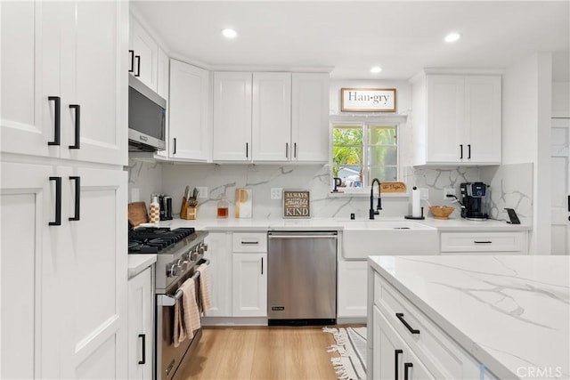 10171 Kukui Dr, Huntington Beach, CA 92646 - kitchen with appliances with stainless steel finishes, white cabinetry, backsplash, light stone counters, and recessed lighting