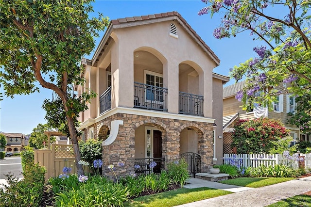 81 Mercantile Way, Ladera Ranch, CA 92694 - mediterranean / spanish-style house featuring a balcony, stone siding, stucco siding, and a fenced front yard