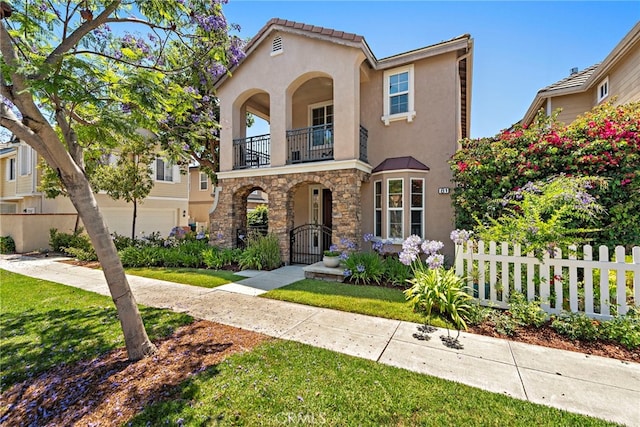 81 Mercantile Way, Ladera Ranch, CA 92694 - mediterranean / spanish home featuring a balcony, a fenced front yard, stucco siding, stone siding, and a gate
