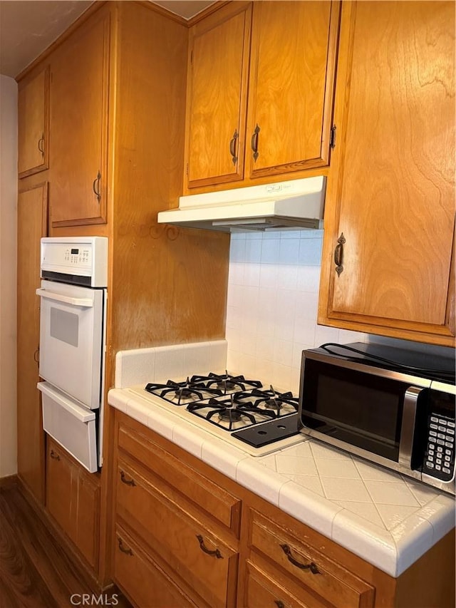 7395 Sage Ave, Yucca Valley, CA 92284 - kitchen featuring a warming drawer, white appliances, under cabinet range hood, tile counters, and brown cabinetry